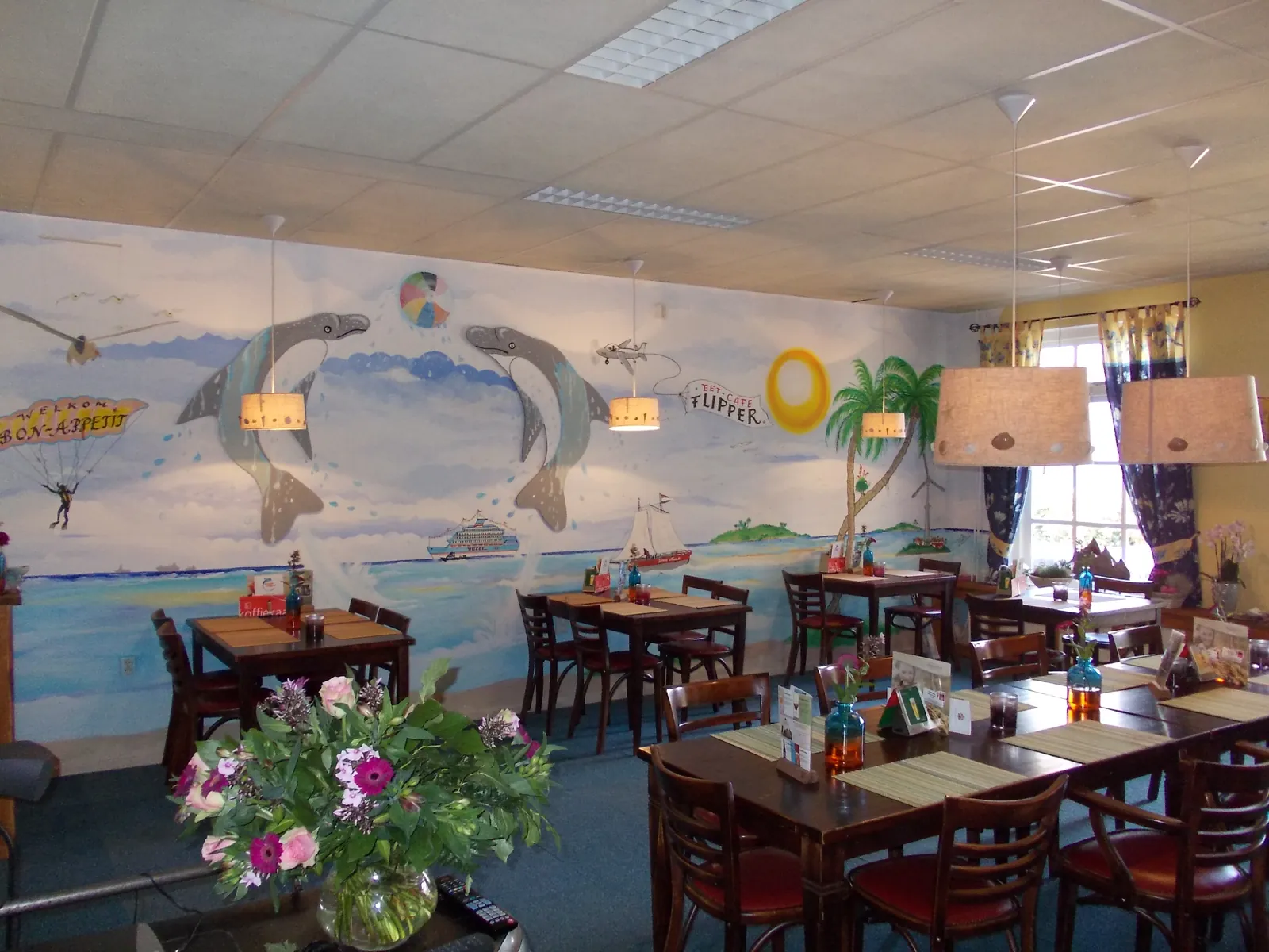 Het interieur van het eetcafé, met een zeewandschildering met dolfijnen